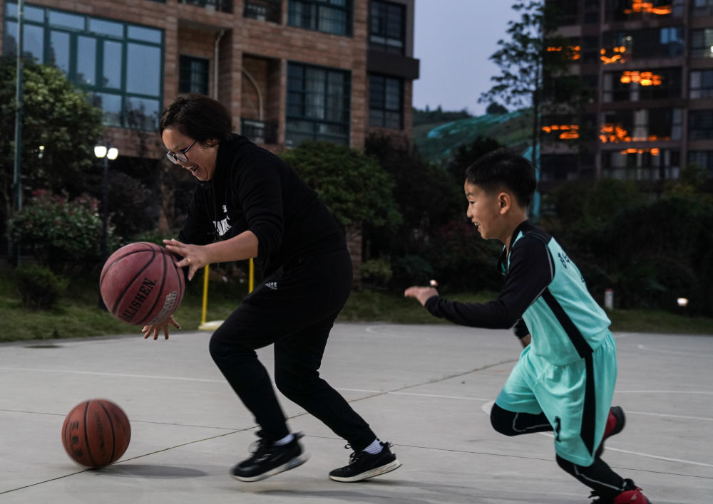 11月2日,曾红在小区的篮球场给儿子展示双手运球.