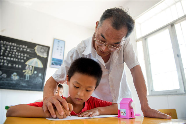 2015年9月8日，在安徽省六安市金寨县梁山小学内，返聘老师叶乃合在给一名孩子辅导作业。新华社记者 郭晨 摄